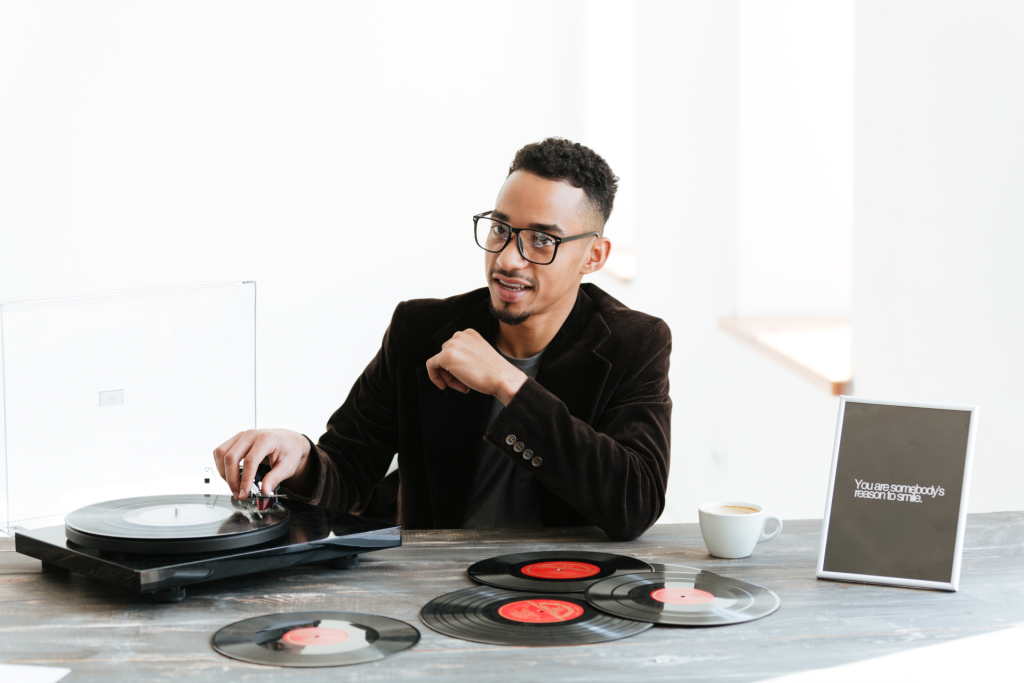 a musician with a cup of coffee and a record sitting at a desk next to a frame with an image saying you are someone's reason to smile